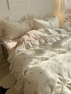 an unmade bed with white sheets and pink flowers on it, in a bedroom