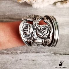 a person's hand is holding two rings with roses on them and the ring has been made out of metal