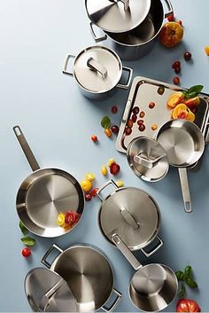 an assortment of stainless steel cookware on a blue surface with fruit and vegetables scattered around it