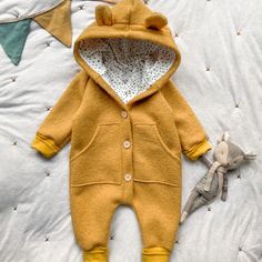 a teddy bear laying on top of a bed next to a baby's clothes