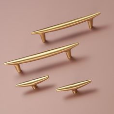 three brass drawer pulls are on a pink surface and one is in the shape of a surfboard