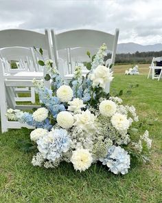 a bouquet of flowers sitting on top of a grass covered field next to white chairs