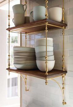 two shelves with plates and cups on them in front of a brick wall that is painted white