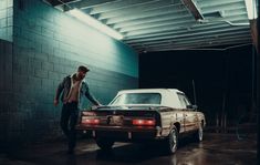 a man standing next to a parked car in a garage with a brick wall behind him