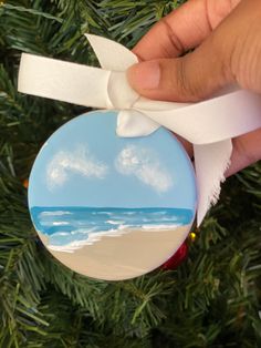 a hand holding a christmas ornament with a beach scene painted on the front