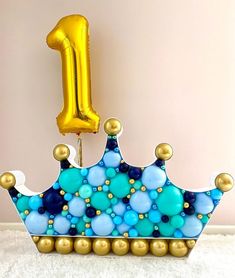 a blue and gold birthday crown with the number one on it's side next to a balloon