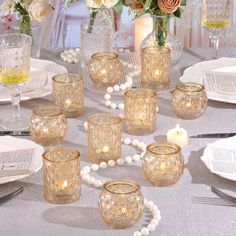 the table is set with candles and glass vases on it, along with other place settings