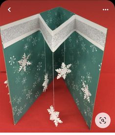 an open christmas card with snowflakes hanging from it's sides on a red background