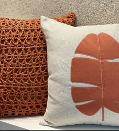 two decorative pillows on a bench in front of a wall with crocheted lace