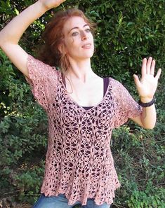 a woman is standing in front of some bushes and holding her hand up to the sky