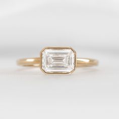 a gold ring with an emerald cut diamond in the center, on a white background