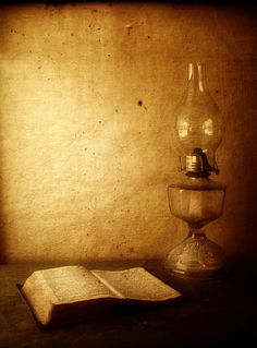 an open book sitting on top of a table next to a glass vase and lamp