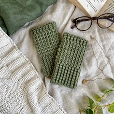 a pair of green knitted mitts next to an open book and eyeglasses