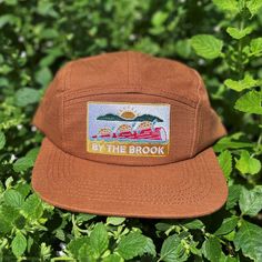 "This \"By The Brook\" flat brim, five panel camper style cap has a turtle and sun embroidered patch and a nylon strap clip closure. Comfortable and classic! * Soft-structured (made of cotton) * Color: Brown Rust * Five panel * Low profile * Nylon strap clip closure * Made by fermentation enthusiasts * The perfect gift for outdoorsy and stylish friends!" Cheap Brown Snapback Hat For Outdoor, Summer Cotton Trucker Hat With Logo Patch, Cotton Snapback Hat With Flat Bill For Camping, Canvas 5-panel Hat For Outdoor Activities, Adjustable Canvas Travel Hat, Cotton Flat Brim Baseball Cap For Camping, Flat Brim Cotton Hat For Camping, Cotton Flat Brim Hats For Camping, Cotton 5-panel Trucker Hat For Outdoor Activities