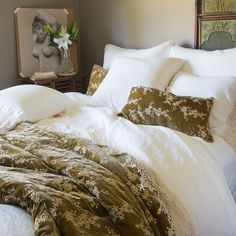 a bed with white and green comforters in a bedroom next to a painting on the wall