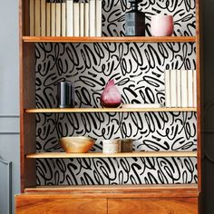 a book shelf with books and vases on it in front of a wallpapered background