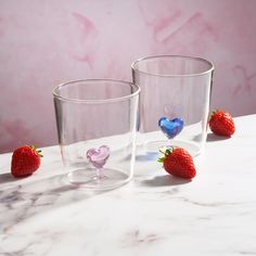 two glasses with hearts and strawberries on a marble countertop next to each other