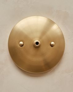 a round brass plate with two holes in the middle on a white wall, and one hole at the center