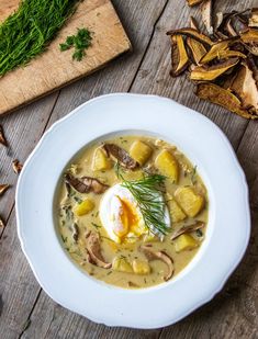 a bowl of soup with an egg in it on a wooden table next to mushrooms and parsley