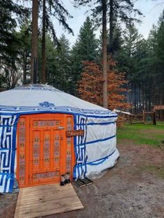 a yurt in the woods with an orange door and blue stripes on it's side