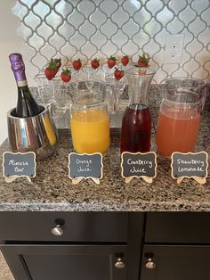 a counter topped with glasses and bottles filled with liquid next to a chalkboard sign that reads, strawberry juice, cranberry juice, lemonade