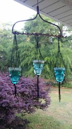 three blue glass vases hanging from a metal stand in front of some purple flowers