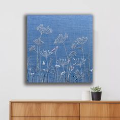 a blue painting on the wall above a dresser with a potted plant next to it