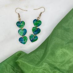 Blue and green handpainted polymer clay hearts dangle from a gold ear wire. Gold dots and a subtle sparkle lend a bit of whimsy to these resin sealed earrings. 💙 Length: approx 2.25" 💚 Weight: less than an ounce 💙 Made from white polymer clay 💚 Handpainted with acrylic paint 💙 sealed with UV resin to add protection and shine Due to variations in computer screens and the handmade nature of this product, colors may vary slightly from the picture. Care: wipe gently with a soft cloth -- 🏡 All Polymer Clay Hearts, Heart Polymer Clay, Clay Hearts, White Polymer Clay, Clay Dangle Earrings, Hand Painted Earrings, Painted Earrings, Green Heart, Gifts For Sports Fans