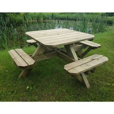 a wooden picnic table sitting on top of a lush green field next to a pond