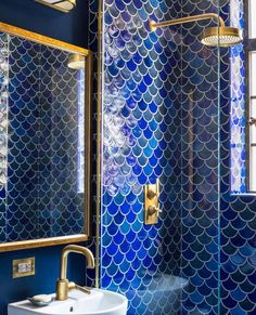 a bathroom with blue and gold tiles on the walls, shower head, sink and mirror