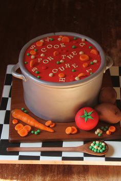 there is a cake that looks like a pot of soup on the table with carrots and peas