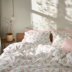 an unmade bed with pink and white flowers on the comforter, next to a window