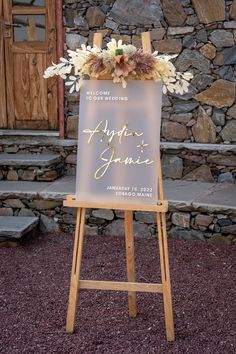 a sign with flowers on it sitting in front of a stone wall next to steps