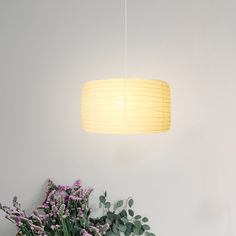 a vase with purple flowers sitting next to a white wall and a light fixture hanging from the ceiling