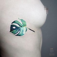 a green leaf tattoo on the side of a woman's right breast is shown