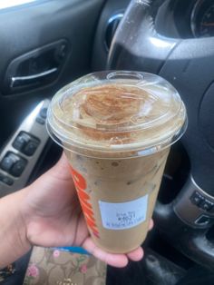 a person holding up a cup of coffee in their hand while sitting in the driver's seat of a car