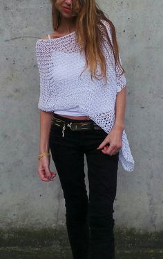 a woman standing in front of a concrete wall wearing black pants and a white top