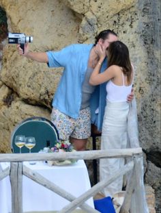 a man and woman kissing while standing next to each other in front of some rocks