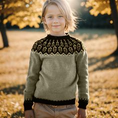 a little boy standing in the grass wearing a sweater