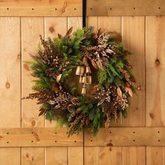 a christmas wreath hanging on the side of a wooden wall with bells and evergreens