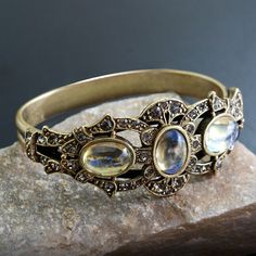 "This rich, unusually impressive bracelet is created from 90 year old stones set into our studio's original sculpture. The bracket is finely detailed and set with premium Swarovski smoke crystal. Three oval stones are vintage beauties from the 1930s which I acquired from a former exporter in Czechoslovakia. The bracket is mounted on a split shank cuff and will comfortably fit 7 to 8\" wrists. Hand burnished warm bronze finish. Entirely made in our Los Angeles studio. Choices:  AMETHYST EMERALD R Victorian Jewelry Bracelet With Jewels, Victorian Jeweled Wedding Bracelets, Collectible Gemstone Bangle Bracelets, Unique Formal Gemstone Bangle, Unique Formal Bangle With Gemstone, Unique Gemstone Bangle For Formal Occasions, Antique Jeweled Bangle, Antique Jeweled Bangle Jewelry, Unique Jeweled Bangle Jewelry