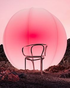 a chair sitting in front of a large pink ball on top of a mountain side