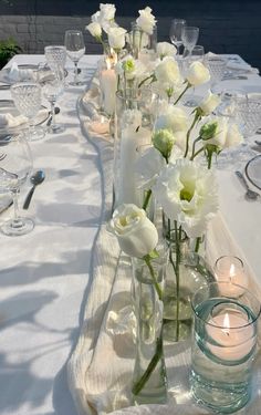 white flowers are in vases on a table with water and candles at the end