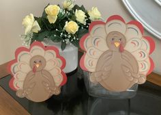 two paper turkeys sitting on top of a table next to a vase with flowers