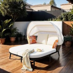 an outdoor daybed with white sheets and pillows on it in the middle of a wooden deck