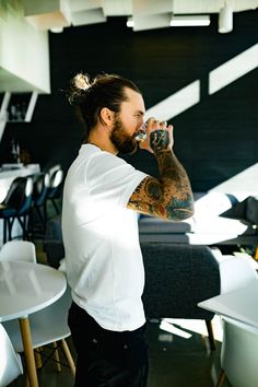 a man with long hair drinking from a bottle while standing in front of a table