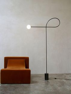 an orange chair sitting next to a black lamp on top of a cement floor in front of a white wall