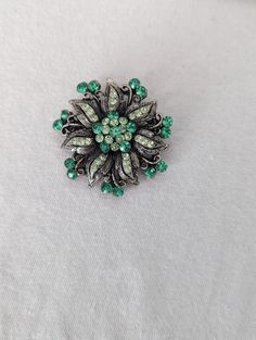 This is a beautiful floral, leaf brooch that is accented with different shades of green rhinestones.  The brooch has multiple shades of green rhinestones in the middle.  Those are surrounded by silver leaves.  More green rhinestones surround the leaves.  This is in great vintage condition. Elegant Green Rhinestone Brooches, Vintage Green Rhinestone Brooches, Green Vintage Rhinestone Brooches, Vintage Green Rhinestone Brooch, Green Flower Shaped Brooch Pins, Green Rhinestone Wedding Brooch, Green Flower Brooch Pins, Green Flower-shaped Brooch Pins, Green Rhinestone Wedding Brooches