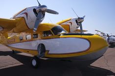 two yellow and white planes parked on the tarmac at an air port with other planes in the background