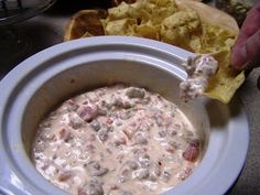 a person dipping some food into a bowl with tortilla chips on the side